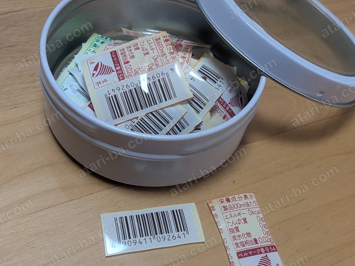 ふた付きの丸い缶ケースにたまったバーコードの束と、手前に置かれた切ったばかりの2枚